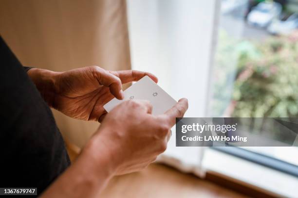 an asian male opens the smart curtain with the remote control in his hand - radiografische afstandsbediening stockfoto's en -beelden