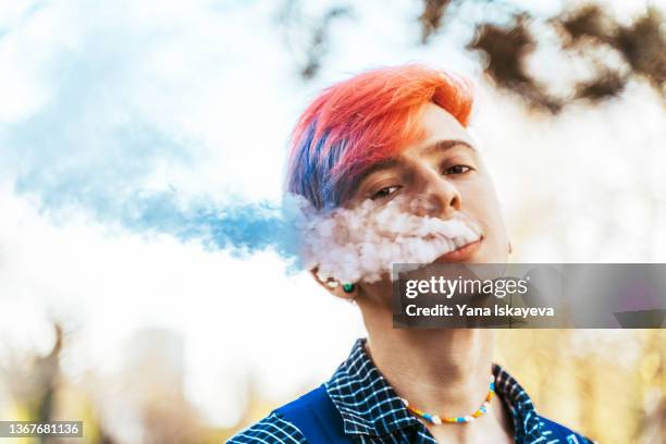 young hipster with purple, very peri colored hair is smoking vape - electronic cigarette smoke stockfoto's en -beelden