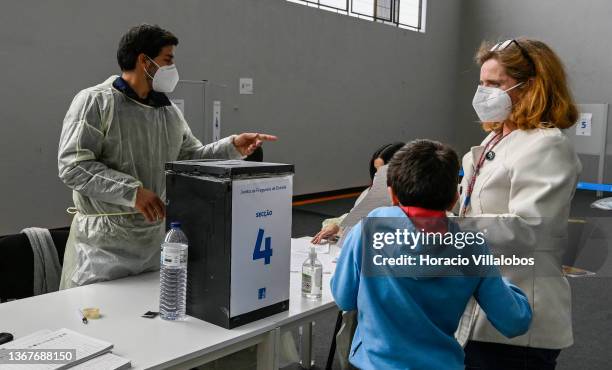 Voting official wears protective gear while helping a mask-clad woman casting her ballot for the country's snap election at a voting station in...