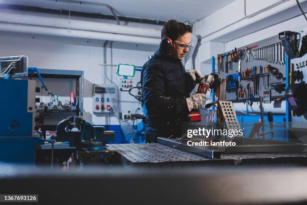 man working in workshop with angle grinder and protective work clothes. - workbench stock pictures, royalty-free photos & images