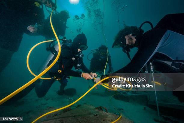 scuba divers installing calbe underwater - coiled wire stock pictures, royalty-free photos & images