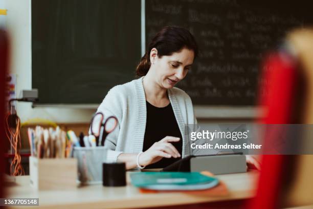 female teacher working on a tablet computer at the desk in a classroom - teacher desk foto e immagini stock