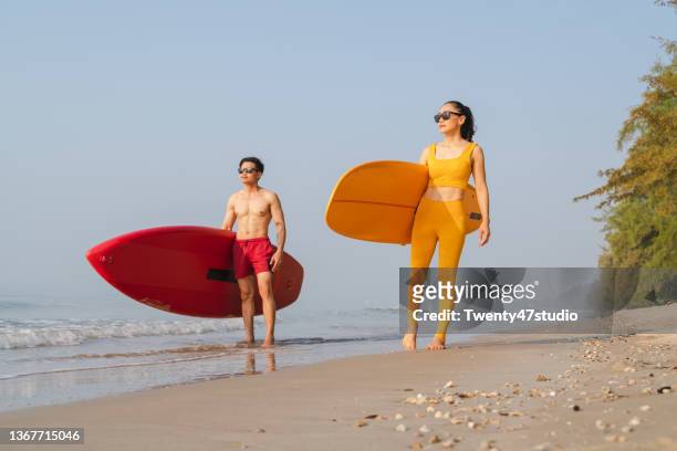 a couple asian surfers carrying the surf board walking on the beach - beach hold surfboard stock-fotos und bilder