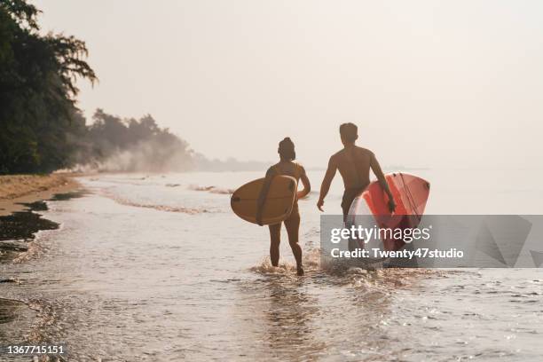 a couple asian surfers carrying the surf board walking on the beach - phuket beach stock-fotos und bilder