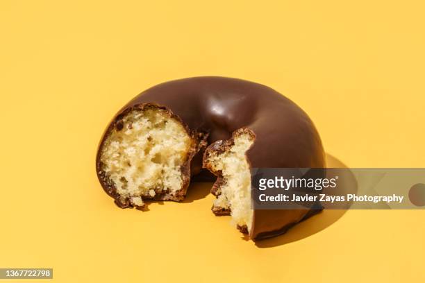 chocolate doughnut on yellow colored background - biting into chocolate stock-fotos und bilder