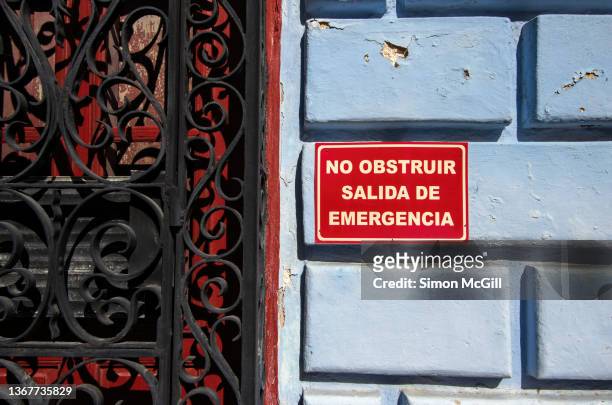 spanish-language sign stating 'no obstruir salida de emergencia' [do not block emergency exit] next to a door on the exterior of a colonial style building - obstruir stock-fotos und bilder
