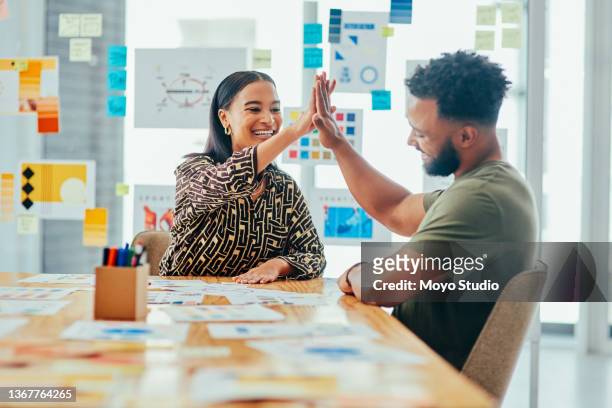 aufnahme von zwei jungen designern, die sich gegenseitig ein high five geben, während sie zusammen in einem büro arbeiten - marketing kommunikation stock-fotos und bilder