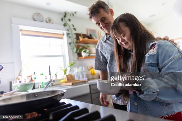 family making breakfast together in kitchen, the daughter has down's syndrome - life skills stock pictures, royalty-free photos & images