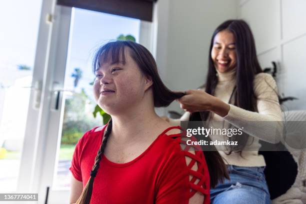 diverse sisters doing each other's hair. one girl has down's syndrome. - adult sibling stock pictures, royalty-free photos & images
