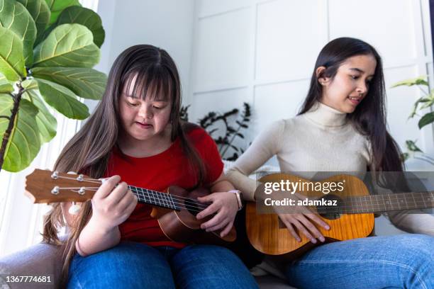 diverse sisters playing eukelele or guitar together. one has down's syndrome. - one friend helping two other imagens e fotografias de stock