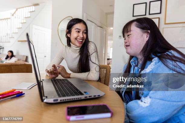 sisters studying together on laptop. one sister has down's syndrome. - one friend helping two other imagens e fotografias de stock