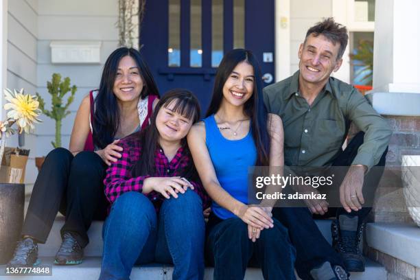 diverse family sitting in front of their home. one daughter has down's syndrome. - step sibling stock pictures, royalty-free photos & images