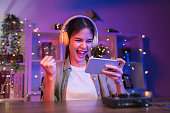 Excited Young Asian woman playing an online game on a smartphone with fists clenched celebrating victory expressing success.