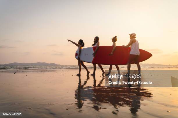 playful asian young people enjoy beach vacation carrying a surfboard on the beach - mid twenties fun stock pictures, royalty-free photos & images