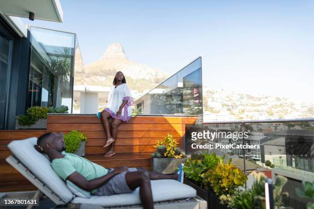 junges afrikanisches paar entspannt auf dachterrasse mit blick auf die berge und die stadt - rooftop pool stock-fotos und bilder