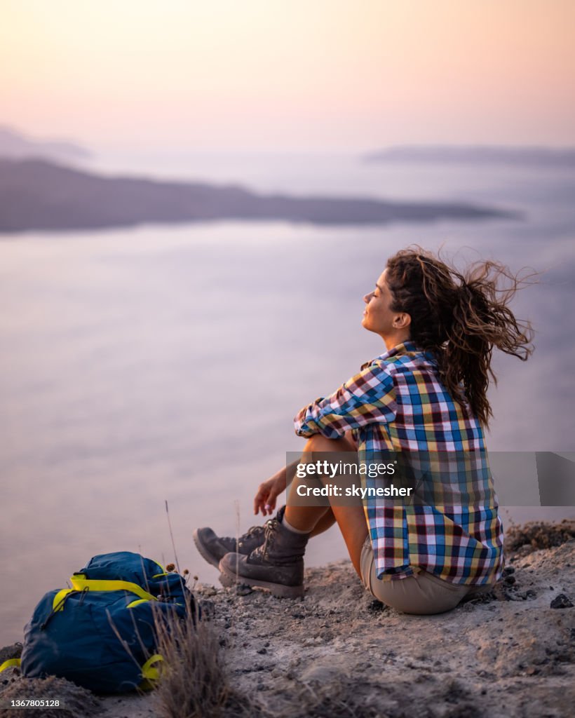 Relaxed woman taking a break from hiking on a hill above the sea.