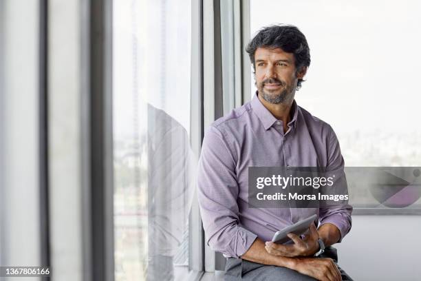 entrepreneur looking through window in office - 45 year old male stock pictures, royalty-free photos & images