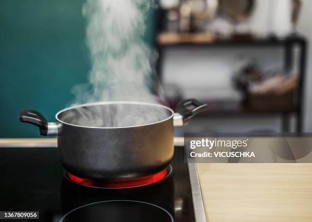 dark cooking pot with water steam on stove at kitchen background - pfanne stock-fotos und bilder