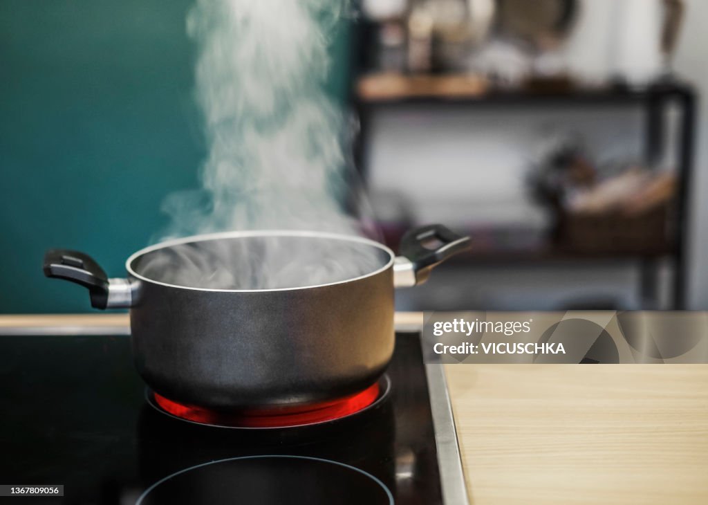 Dark cooking pot with water steam on stove at kitchen background