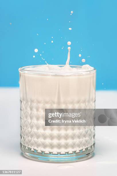 transparent glass with milk and splashes on a pastel blue  and white color background. - milk flowing stock pictures, royalty-free photos & images