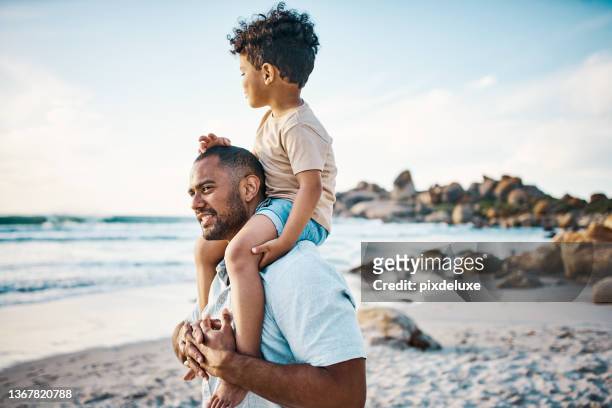 aufnahme eines mannes, der seinen sohn am strand auf den schultern trägt - father and son playing stock-fotos und bilder