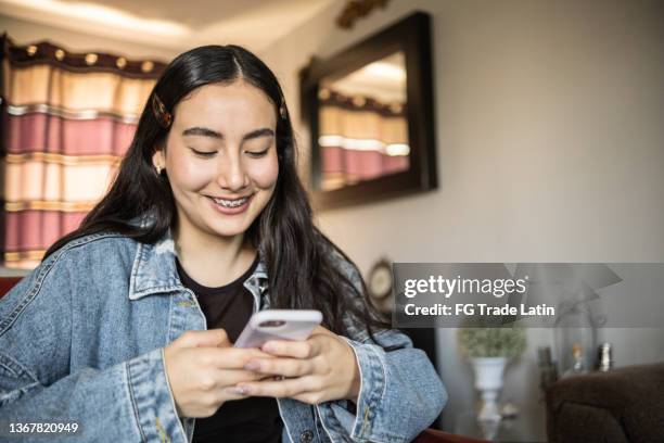 teenage latin girl using smartphone at home - candid forum stockfoto's en -beelden