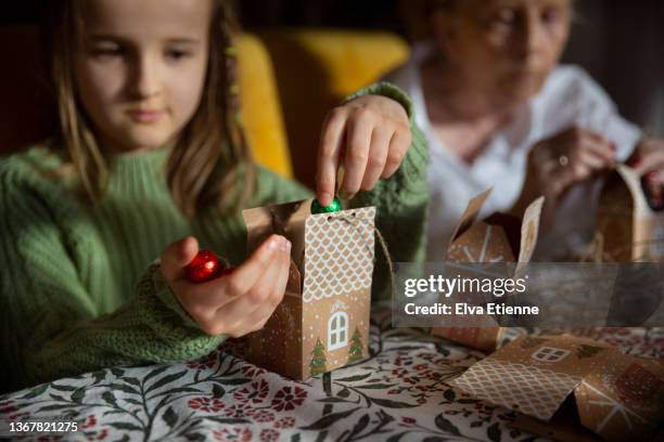 child and grandmother filling diy advent calendar boxes with foil wrapped chocolates at a dining table - child with advent calendar 個照片及圖片檔