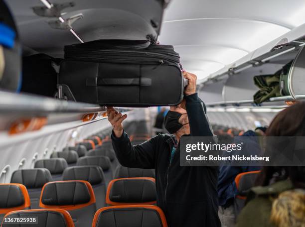 JetBlue passenger puts his carry-on luggage into an overhead compartment January 28, 2022 at John F. Kennedy International Airport in New York City.