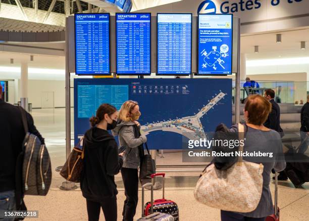 Airline passengers check the departure and arrival board January 28, 2022 at John F. Kennedy International Airport in New York City.