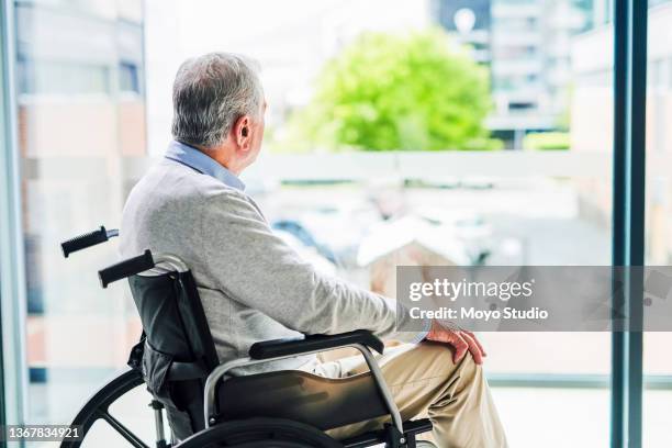 shot of a senior man looking out of a window while sitting in a wheelchair at a clinic - grief loss stock pictures, royalty-free photos & images