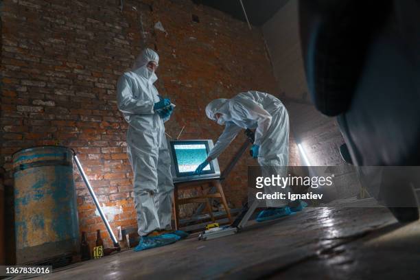 police criminologists in protective suits  taking fingerprints at the crime scene in warehouse, low angle - film and television screening stockfoto's en -beelden