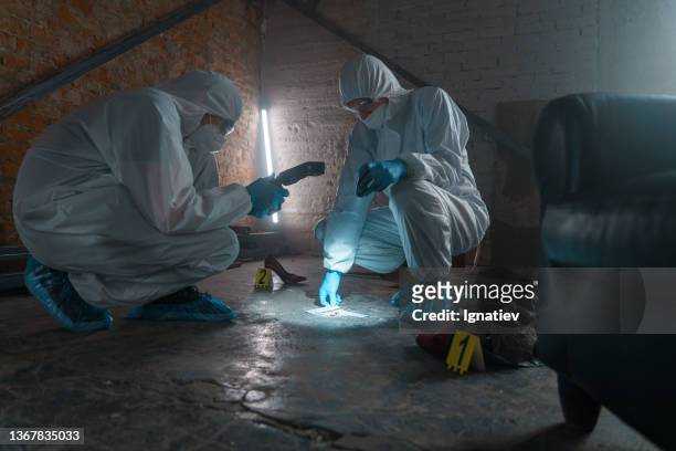 criminólogos en trajes protectores con cámara tomando fotos de evidencia física en una luz de linterna - crime fotografías e imágenes de stock