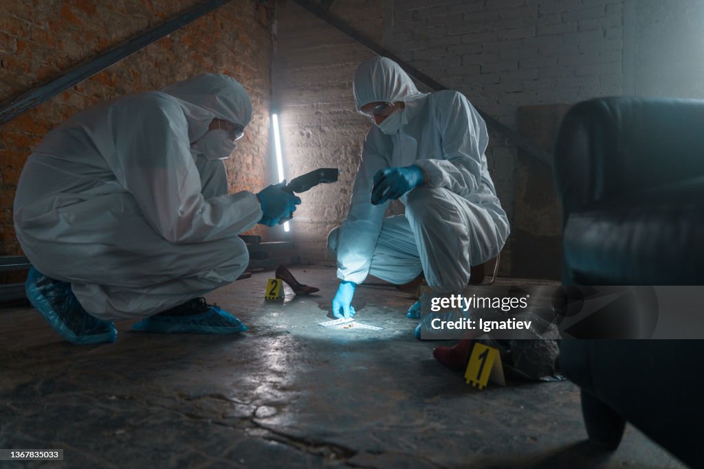 Criminologists in protective suits with camera taking photos of physical evidence in a flashlight light