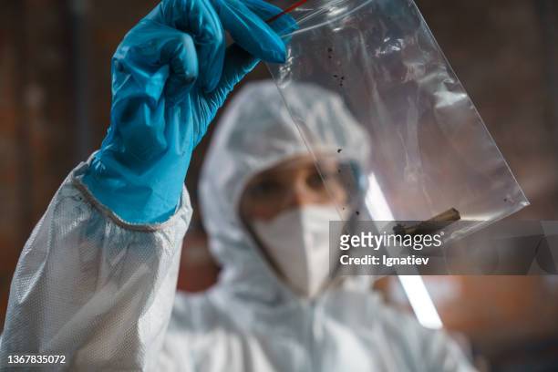 young criminologist in protective suit and mask looks at cigarette butt in a plastic bag - video reviewed stock pictures, royalty-free photos & images