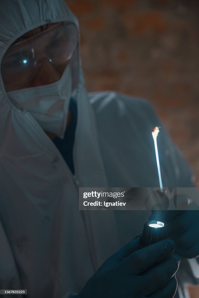 Criminologist with a cotton swab with blood, illuminated by flashlight