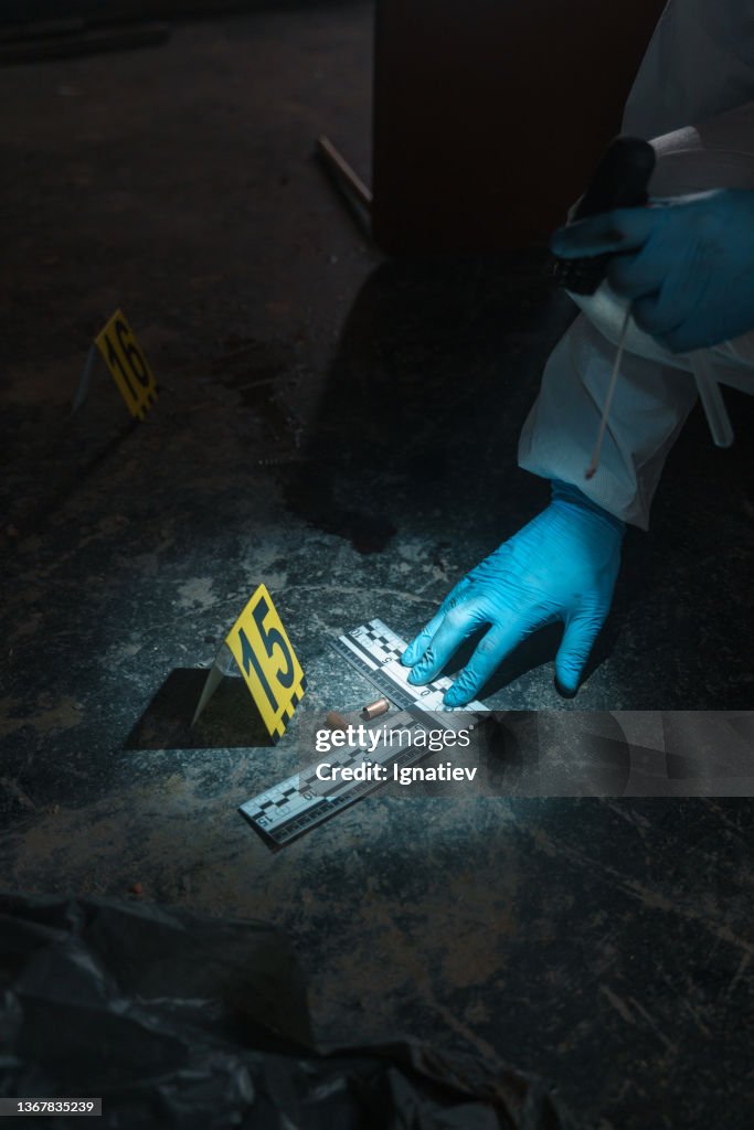 Crime scene number on the floor near two bullets with criminalistic ruler and a criminologist hand in glove