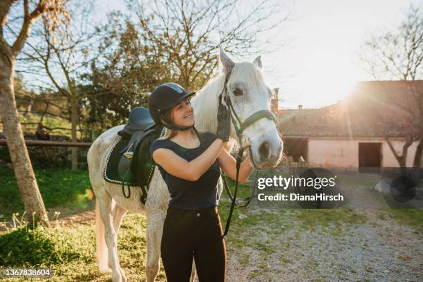 beautiful blond woman embracing her horse after riding training at a rustic stable outdoors in majorca - paarden stockfoto's en -beelden