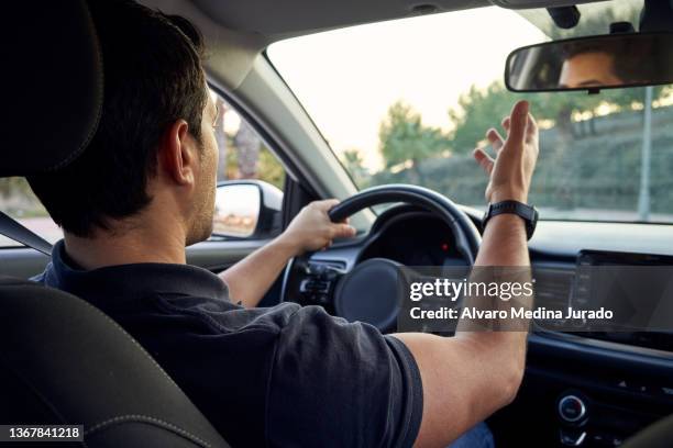 close up side view shot from inside a car of a young unrecognizable hispanic man discussing with other drivers while driving his car. - man driving anxiously stock-fotos und bilder