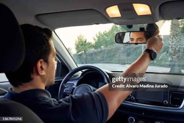 rear view from inside a car of a young hispanic man adjusting his car's rear view mirror. - car rear view mirror stock pictures, royalty-free photos & images