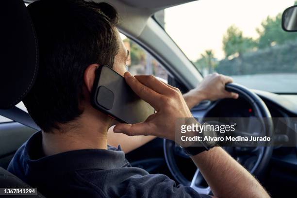 rear view of a young unrecognizable hispanic man talking on a smartphone while driving his car. - steering wheel stockfoto's en -beelden