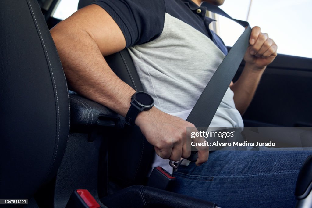 Unrecognizable young Hispanic man buckling his seat belt inside his car.