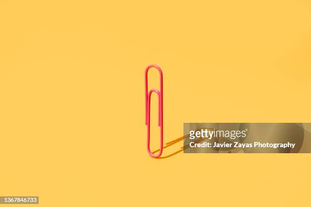 pink paper clip on yellow background - paperclip imagens e fotografias de stock