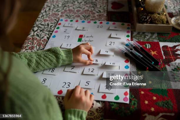 child opening the card window of a simple, homemade advent calendar on a dining table - child with advent calendar stock pictures, royalty-free photos & images