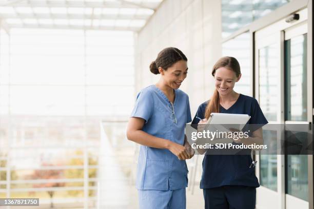 standing in walkway, female nurses discuss medical chart - nurse smiling stock pictures, royalty-free photos & images