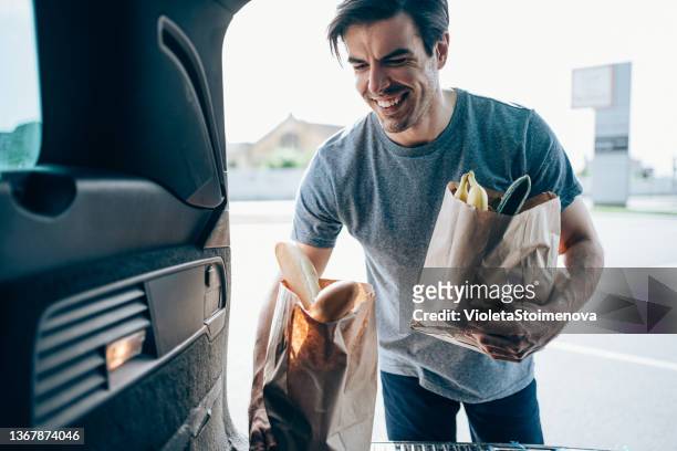 young man putting groceries in a car trunk. - unloading stockfoto's en -beelden