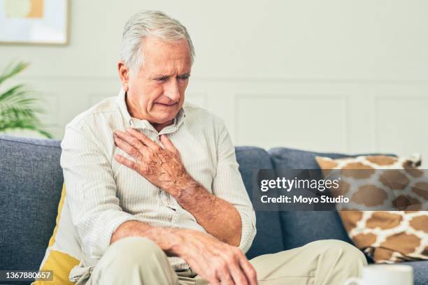 foto de un hombre mayor sosteniendo su pecho con dolor mientras estaba sentado en casa - human heart fotografías e imágenes de stock