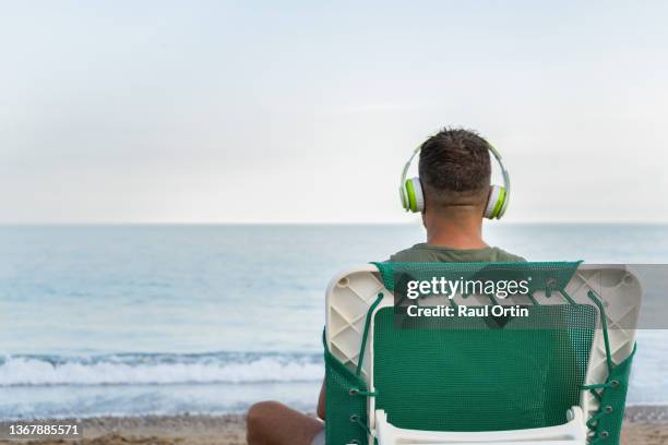 back view of a man listening music relaxing on deck chair at beach. - beach music stock pictures, royalty-free photos & images