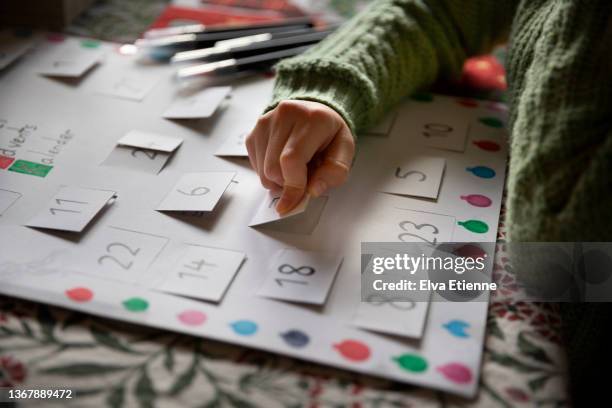 close up of a child opening the window of a simple, homemade, card advent calendar on a dining table - advent calendar paper stock pictures, royalty-free photos & images