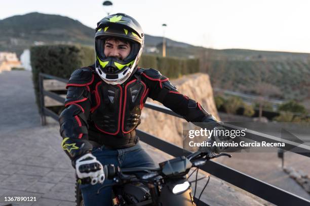 young man in his thirties on a sunny day poses with his electric motorcycle in a viewpoint at sunset - motociclista fotografías e imágenes de stock