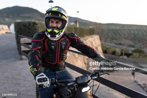 young man in his thirties on a sunny day poses with his electric motorcycle in a viewpoint at sunset - motorcycle biker photos et images de collection